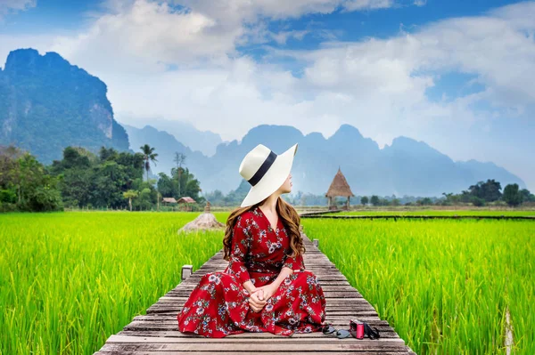 Mujer joven sentada en el camino de madera con campo de arroz verde en Vang Vieng, Laos . —  Fotos de Stock