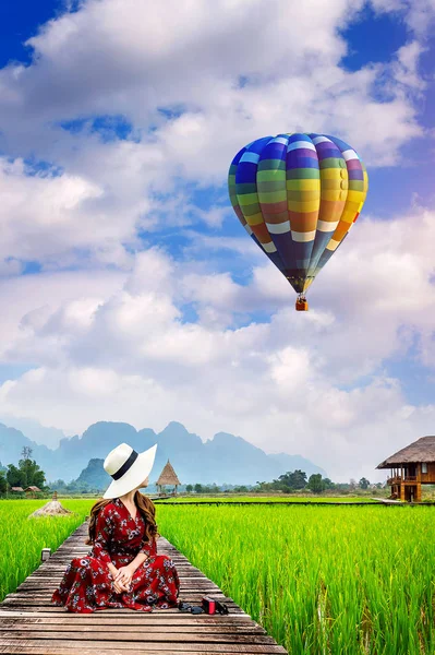 Jovem olhar para o balão e sentado no caminho de madeira com campo de arroz verde em Vang Vieng, Laos . — Fotografia de Stock