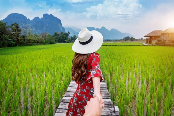 Wanita memegang tangan pria dan membawanya ke jalan Wooden dan sawah hijau di Vang Vieng, Laos . — Stok Foto