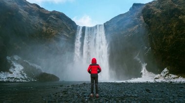 İzlanda 'da Skogafoss şelalesi. Kırmızı ceketli adam Skogafoss şelalesine bakıyor..