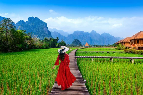 Jonge vrouw lopen op houten pad met groene rijst veld in Vang Vieng, Laos. — Stockfoto