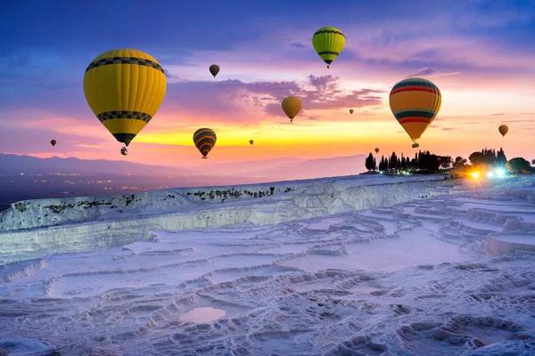 Türkiye 'nin Pamukkale kentinde gün batımında sıcak hava balonları ve doğal travertin havuzları.