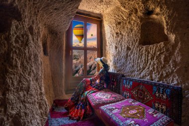 Mağara evinde oturan ve Goreme, Kapadokya, Türkiye 'de manzaralı pencerelere bakan kadın.
