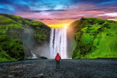 İzlanda 'da Skogafoss şelalesi. Kırmızı ceketli adam Skogafoss şelalesine bakıyor..