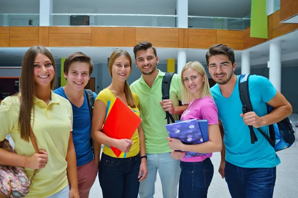 Kitaplar ve klasörlerle Üniversitesi salonunda ayakta altı mutlu öğrenciler