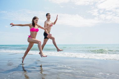 Genç çift sahilde koşup zıplarken birlikte eğleniyor. 