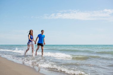 Genç çift sahilde koşup zıplarken birlikte eğleniyor. 