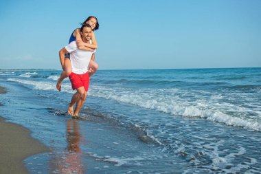  Sahilde sırtında kadın taşıyan bir adam.