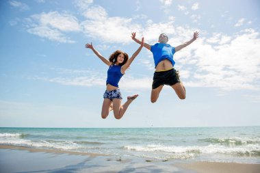 Genç çift sahilde koşup zıplarken birlikte eğleniyor. 
