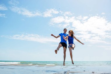 Genç çift sahilde koşup zıplarken birlikte eğleniyor. 