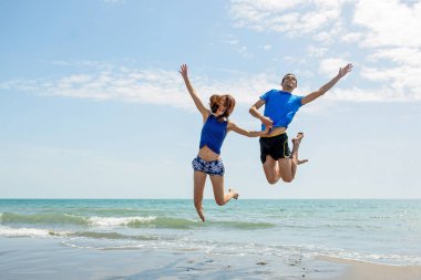 Genç çift sahilde koşup zıplarken birlikte eğleniyor. 