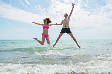 Genç çift sahilde koşup zıplarken birlikte eğleniyor. 