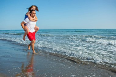  Sahilde sırtında kadın taşıyan bir adam.