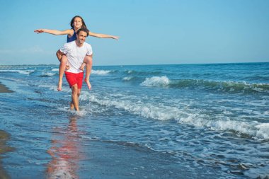  Sahilde sırtında kadın taşıyan bir adam.