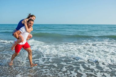  Sahilde sırtında kadın taşıyan bir adam.