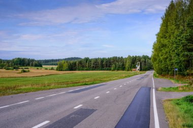Mavi gökyüzünün arka planında bulutlu asfalt yol. Finlandiya 'nın tipik manzarası