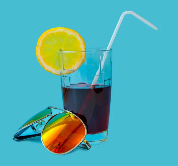 Taze meyve suyu cam sarı limon ve mavi bir arka plan üzerinde güneş gözlüğü saman bir dilim. Moda pastel yaz tasarım stil