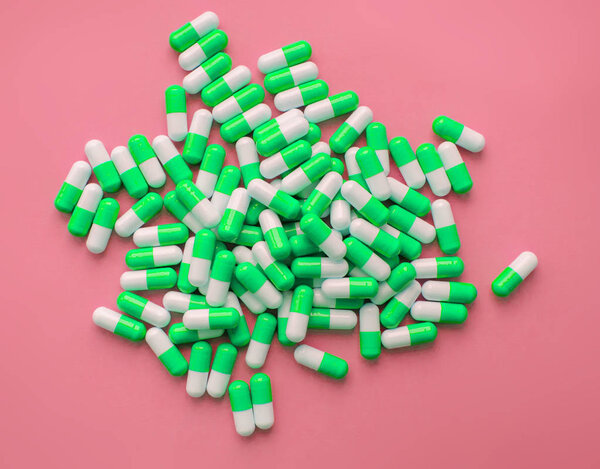 green and white pills or capsules lies in a rows on pink background close up wallpaper concept design