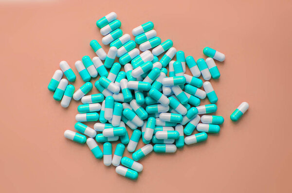Pile of blue capsules of pills on a pink pastel background top view. Medicine Health Pharmacy Pharmacology Concept