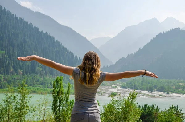 beautiful girl with outstretched arms on the background of high mountains near the coast of the lake