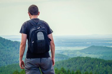 Sırt çantalı genç adam dağda duruyor.