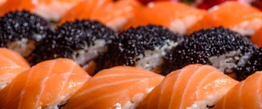 Karanlık bir arka planda servis edilen çeşitli suşi çeşitleri.