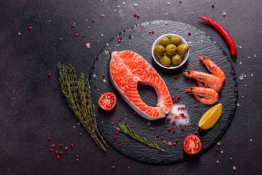 Çiğ alabalık, kırmızı balık bifteği, otlar, limon ve koyu bir arka planda zeytinyağı ile servis edilir.