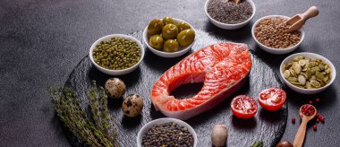 Çiğ alabalık, kırmızı balık bifteği, otlar, limon ve koyu bir arka planda zeytinyağı ile servis edilir.