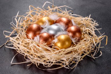 Yuvadaki Paskalya altın yumurtaları, bayram hazırlıkları. Koyu renkli arka planda yuvadaki altın yumurtalar.