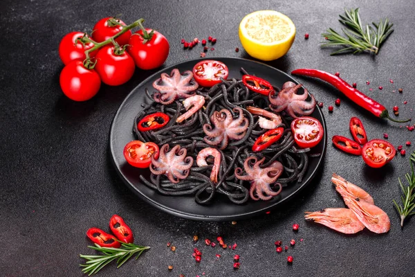 Black seafood pasta with shrimp, octopus and mussels on black background. Mediterranean gourmet food. Black pasta with octopus on a black stone plate