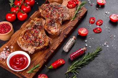 Kemiklerin üzerinde taze, lezzetli, sebze ve baharatlı biftek ve koyu bir arka plan. Pork sulu biftek ızgarası karanlık masada.