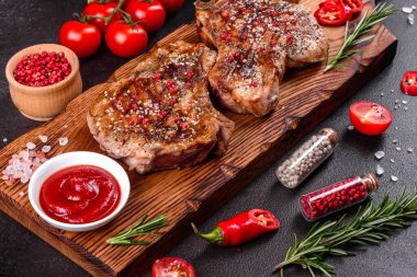 Kemiklerin üzerinde taze, lezzetli, sebze ve baharatlı biftek ve koyu bir arka plan. Pork sulu biftek ızgarası karanlık masada.