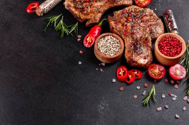 Kemiklerin üzerinde taze, lezzetli, sebze ve baharatlı biftek ve koyu bir arka plan. Pork sulu biftek ızgarası karanlık masada.