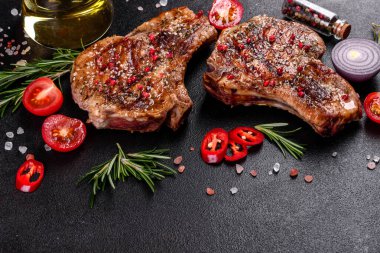 Kemiklerin üzerinde taze, lezzetli, sebze ve baharatlı biftek ve koyu bir arka plan. Pork sulu biftek ızgarası karanlık masada.
