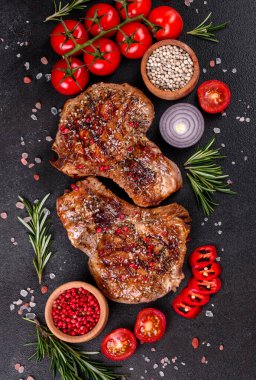 Kemiklerin üzerinde taze, lezzetli, sebze ve baharatlı biftek ve koyu bir arka plan. Pork sulu biftek ızgarası karanlık masada.