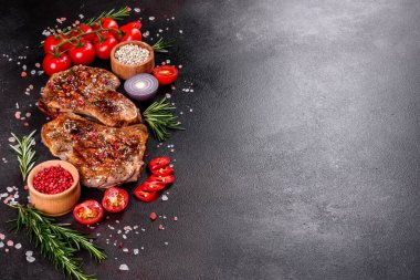 Kemiklerin üzerinde taze, lezzetli, sebze ve baharatlı biftek ve koyu bir arka plan. Pork sulu biftek ızgarası karanlık masada.