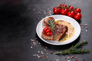 Kemiklerin üzerinde taze, lezzetli, sebze ve baharatlı biftek ve koyu bir arka plan. Pork sulu biftek ızgarası karanlık masada.