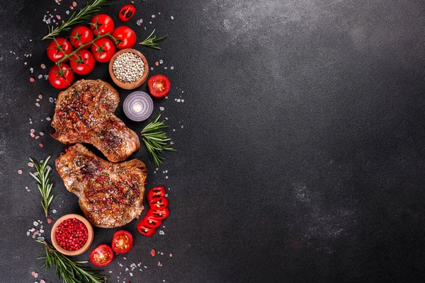 Kemiklerin üzerinde taze, lezzetli, sebze ve baharatlı biftek ve koyu bir arka plan. Pork sulu biftek ızgarası karanlık masada.