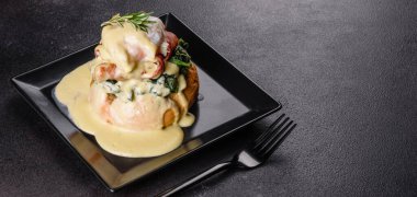 Benedict yumurtaları ya da Floransa usulü yumurtalar kafede siyah bir tabakta. Kızarmış İngiliz keki üzerine yumurtalı Benedict.