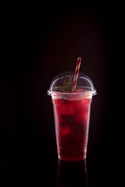 Soğuk limonatayı çileklerle, nane şekeriyle ve buzlu siyah arka planda kapaklı plastik bardakla tazeliyorum.