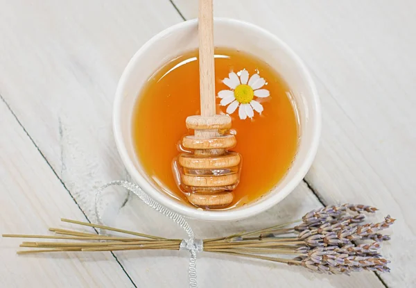 Bowl filled with flower honey and spoon with a cup of tea with c