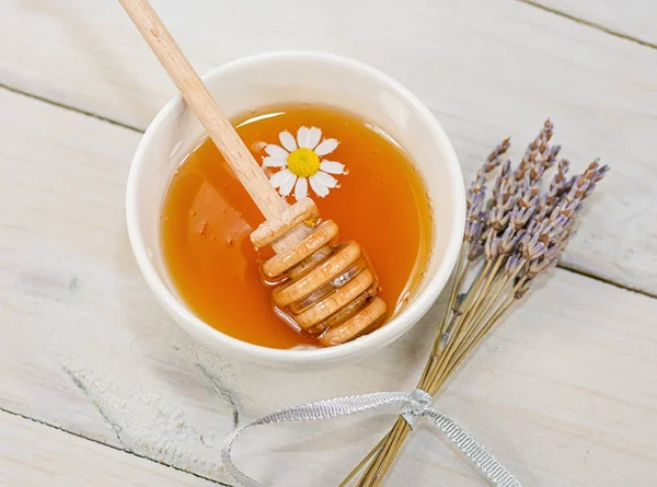 Bowl filled with flower honey and spoon with a cup of tea with c