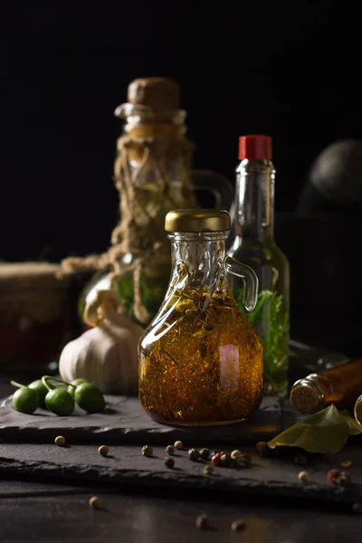 Jugs with extra virgin olive oil on a black stone board surrounded by spices, garlic and olives. Selective focus. The concept of a healthy natural food. Low key, — Stock Photo, Image