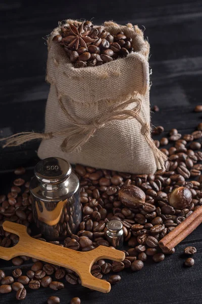 Kahve çekirdekleri ve siyah ahşap arka plan üzerinde çul çanta içinde baharatlar.
