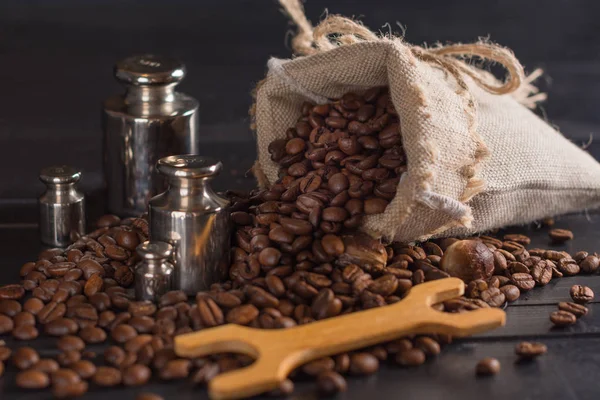 Kahve çekirdekleri ve siyah ahşap arka plan üzerinde çul çanta içinde baharatlar.