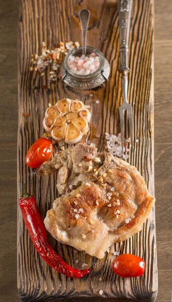 Gegrilltes Schweinefleisch mit Kirschtomaten und Knoblauch auf Holzbrett. Ansicht von oben. Kopierraum. — Stockfoto