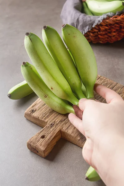 Manojo de plátanos verdes maduros. Fondo gris. La mano del hombre —  Fotos de Stock