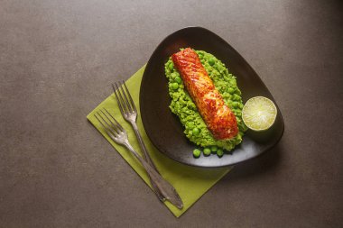 Kahverengi bir plaka üzerinde bezelye püresi ile ızgara somon. Gri arka planı.