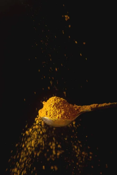 Cuillère en métal avec curcuma jaune. Des épices tombantes. Arrière-train noir — Photo