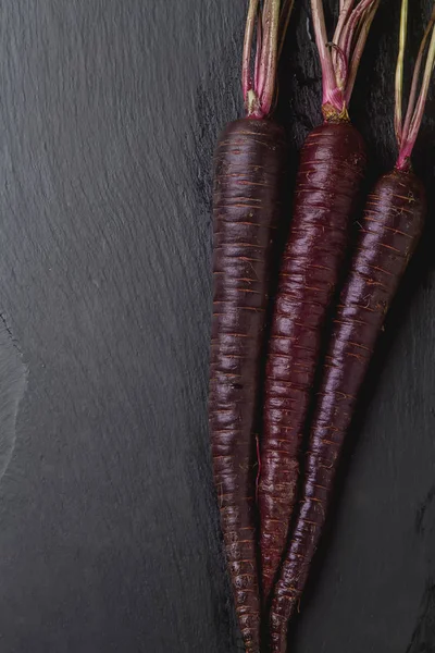 Ripe black carrots. Dark stone background. Autumn harvest. Top v